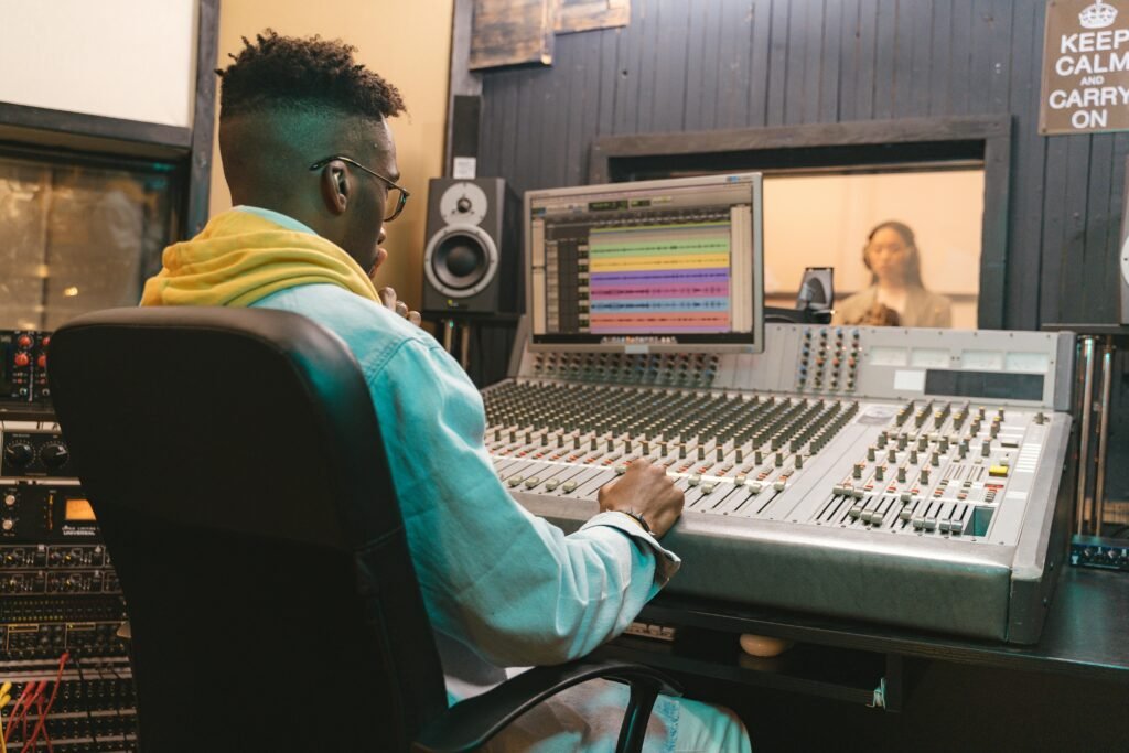 A music producer works attentively at an audio mixing console in a recording studio.